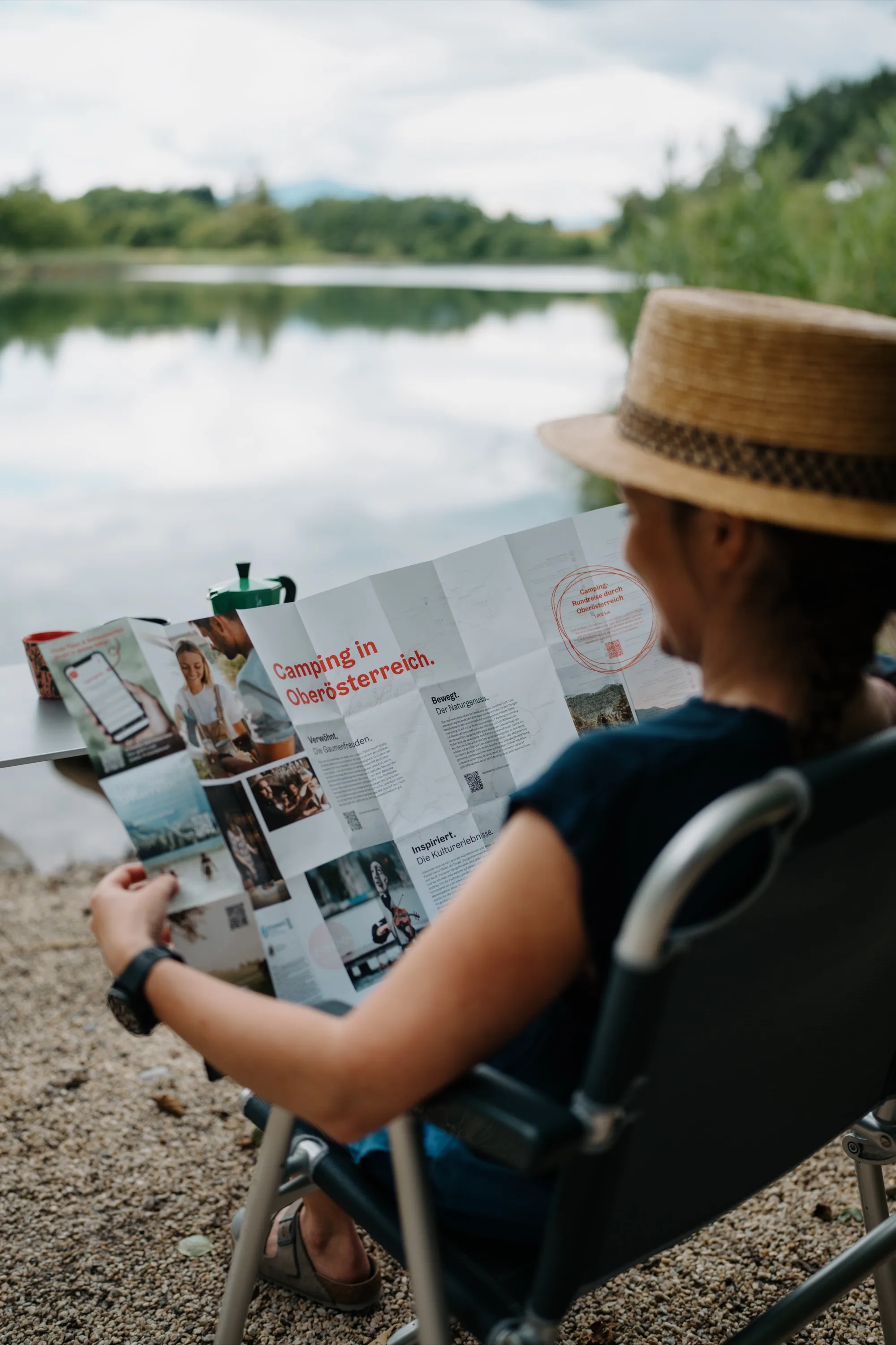 Camping in Oberösterreich – Frau mit Strohhut liest s-format Faltkarte am See