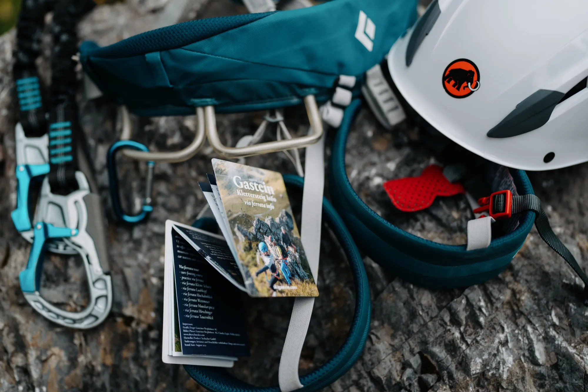 Klettersteig-Guide Gasteinertal Twin-Card neben Kletterausrüstung – Helm, Karabiner und Klettergurt auf Felsen
