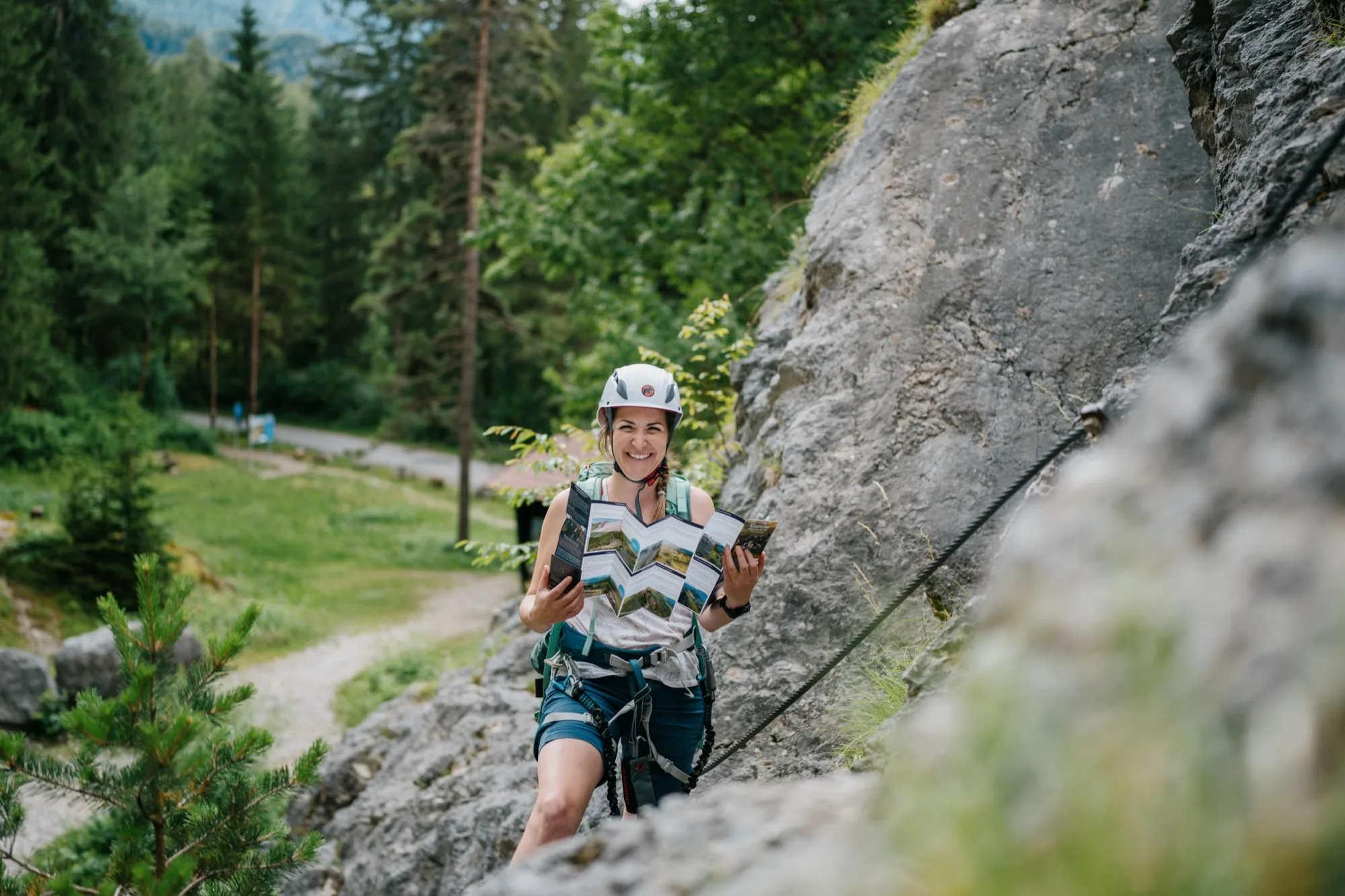 Kletterin zeigt aufgefalteten Klettersteig-Guide Gasteinertal am Klettersteig mit Bergpanorama im Hintergrund