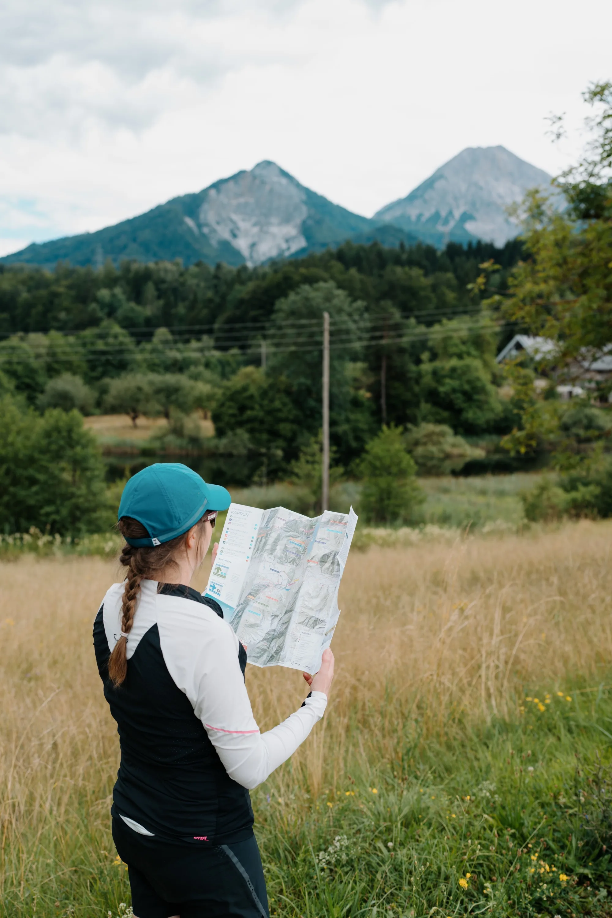 Laufkarte Zell am See-Kaprun – Läuferin studiert Faltkarte vor Bergpanorama mit Wiese